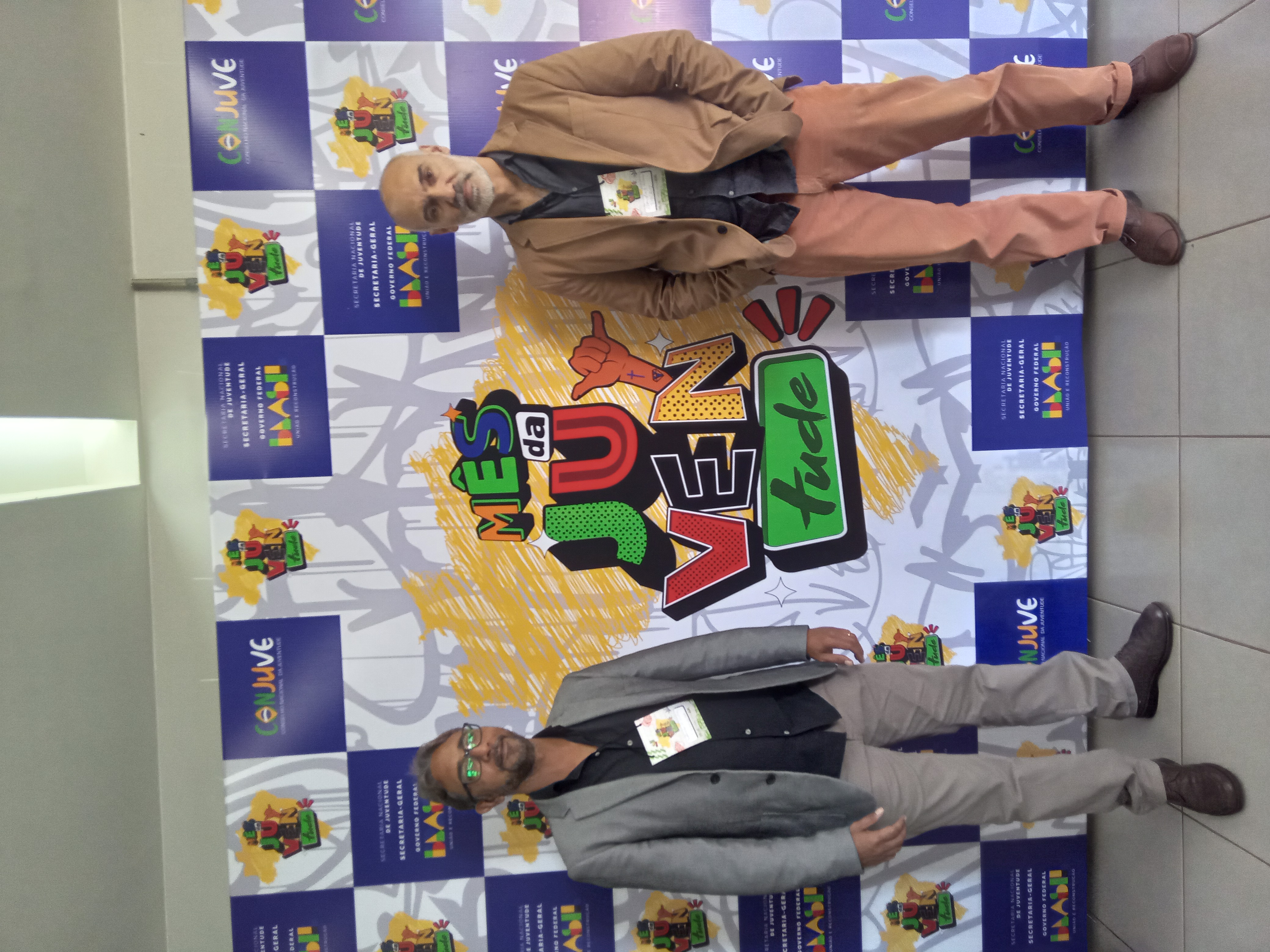 pesquisadores da Escola Politècnica de Saúde Joaquim Venâncio da Fiocruz, posam ao lado de cartaz do evento, em Brasília.