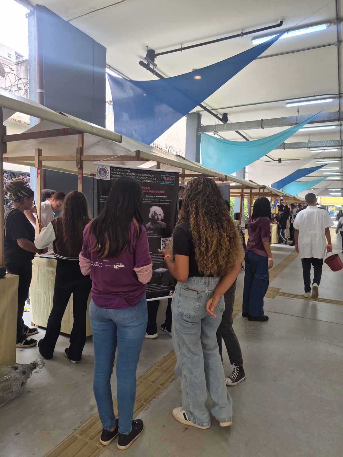 Pessoas circulam entre estandes de projetos durante mostra científica em corredor de exposição.