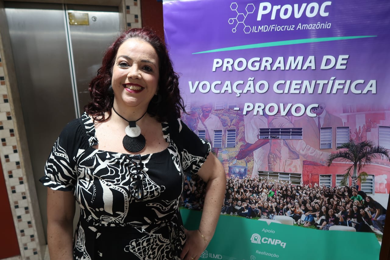 coordenadora da rede provoc, Cristiane Braga, na frente do banner do evento de acolhimento de estudantes do Provoc Amazônia.