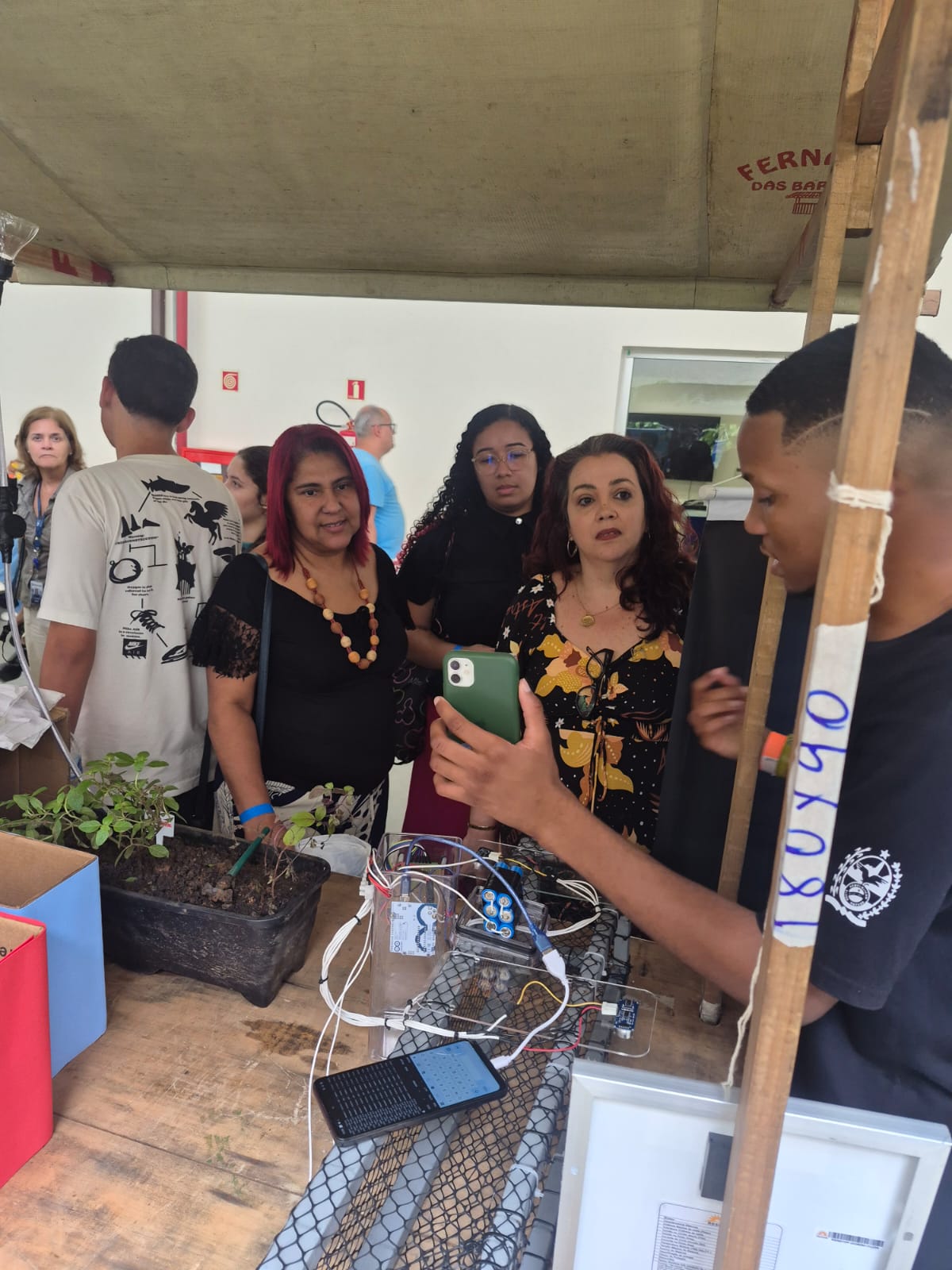 Estudante apresenta projeto de monitoramento de plantas com sensores e placa solar em feira científica.