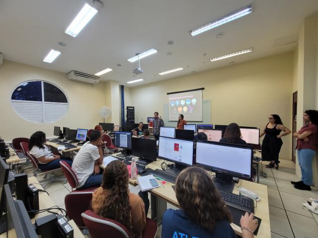 estudantes sentados de frente a computadores e os professores na frente explicando o conteúdo.o.