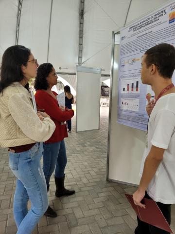 aluno apresenta seu poster para duas avaliadoras na Tenda.